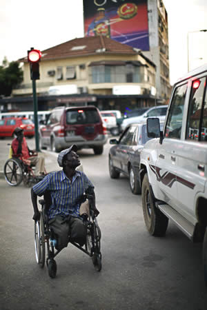 Beggar in wheelchair approaching a car.