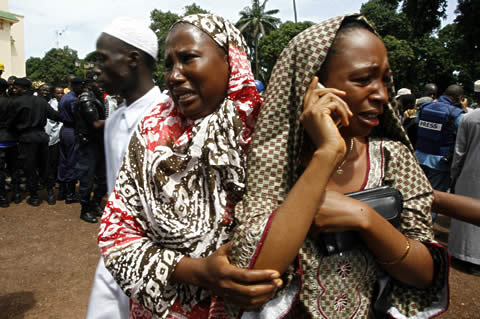 Women cry after identifying the body of a relative killed during an army massacre of protesters in Guinea