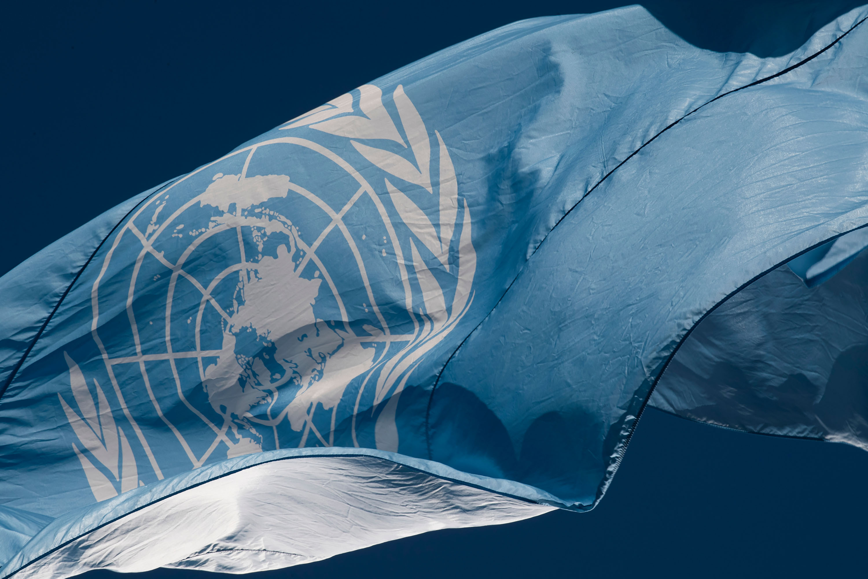 The flag of the United Nations flying -- white emblem on a light blue field.