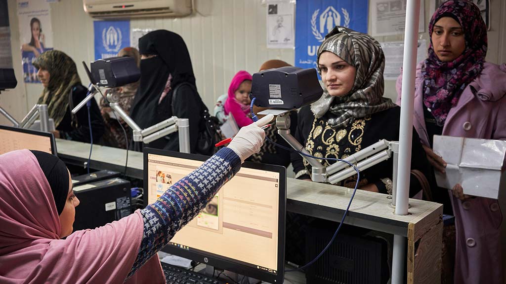 A Syrian refugee, second right, has her identity checked with iris recognition technology before queuing to receive winter cash assistance at Zaatari refugee camp, Jordan. Photo: UNHCR/David Azia