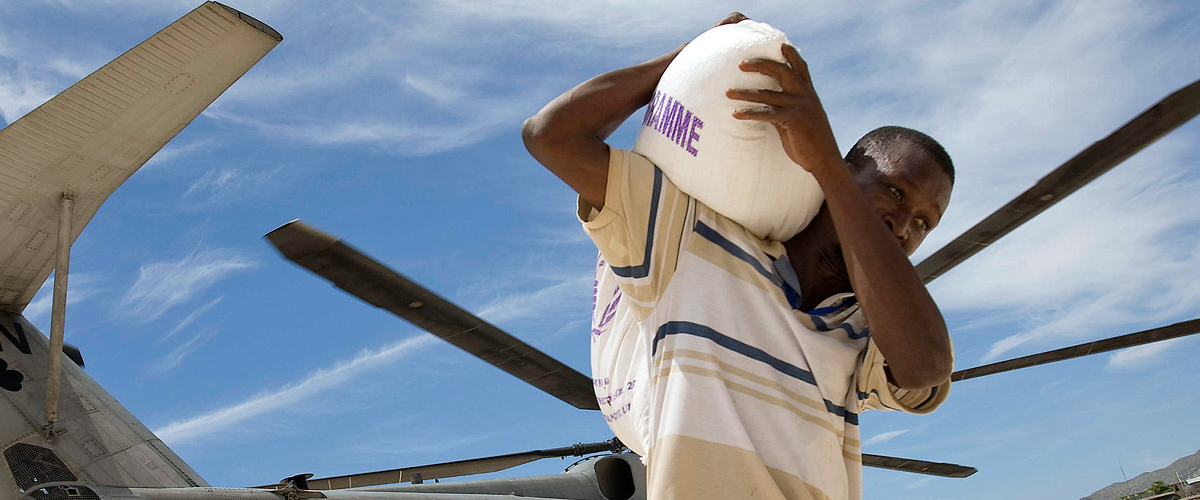 Un travailleur humanitaire transporte un sac d’approvisionnement de denrées alimentaires du Programme alimentaire mondial (PAM) pour des populations touchées par une tempête.