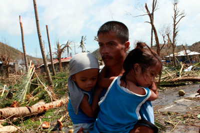 Un hombre lleva en brazos a sus hijos en Tacloban, Leyte, Filipinas, tras el paso del super tifón Haiyan (conocido localmente como Yolanda). Foto: UNICEF