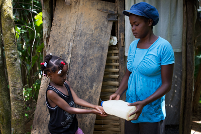 27 year old Celianne Jean pours treated water on her daughter's hands after using a household latrine in Petit Bourg de Borgne, a remote village in the mountains East of Cap Haitian, in the North of Haiti. This is one of the several latrines built by community in the area after receiving CLTS (Community Led Total Sanitation) training on good hygiene practices and the importance of building and using latrines to avoid to contaminate the water by defecating in open fields.