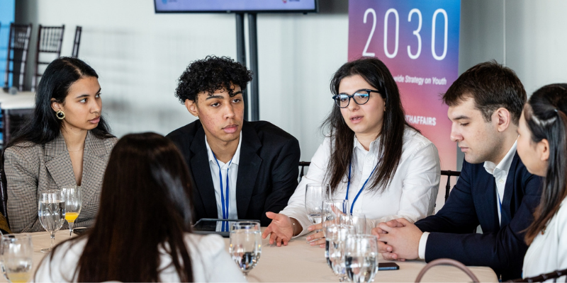 Five young people seated at a table actively engaged in conversation