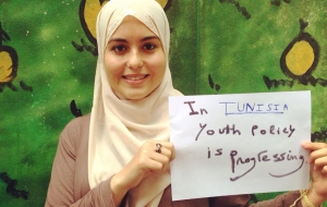 A young woman in a headscarf holds up a sign that says "In Tunisia, youth policy is progressing"