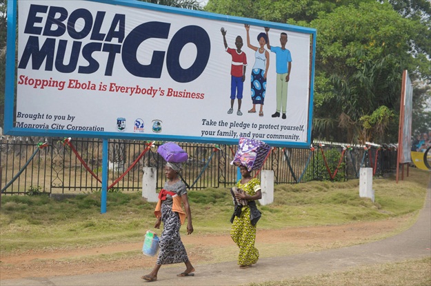Two women in Monrovia, Liberia, walk in front of a billboard, which says "Ebola must go. Stopping Ebola is Everybody's Business." File Photo: UNMIL/Emmanuel Tobey