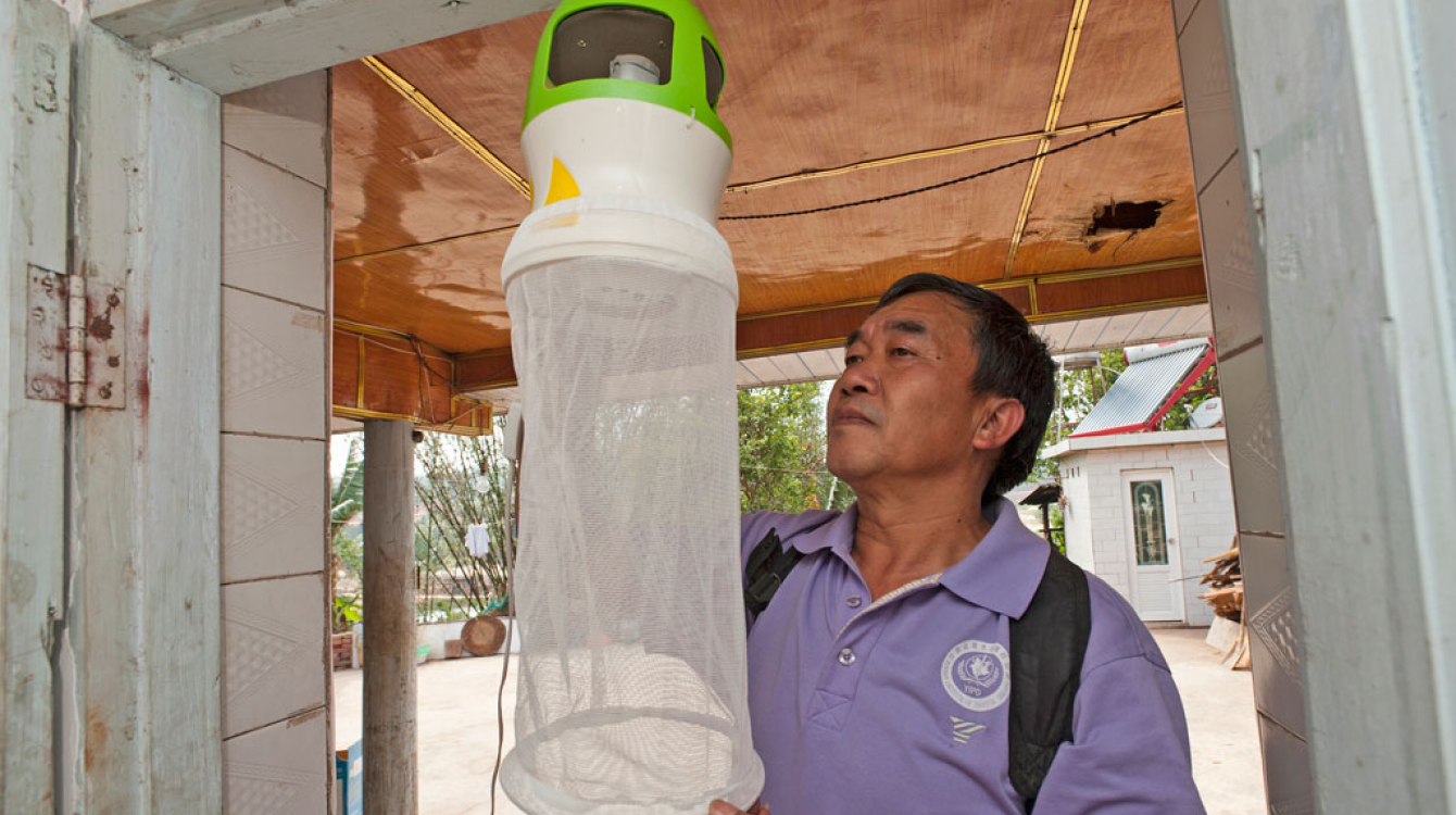 Health worker checking the installation of an anti-mosquito device at the entrance of a house. Such devices may help to trap mosquitoes, flies and insects. Photo: WHO/TDR/S. Lim