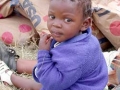 Child sitting amidst sacks of relief grain in Lesotho: Emergency aid is vital, but “just shipping in food is not enough,” says UN Secretary-General Kofi Annan: Poverty and other causes of famine must also be addressed.  Photograph: WFP / R. Lee