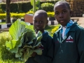 A student holding an SDG badge (top). Students holding vegetables from the school garden (left). Brian (WEYE Clean Energy) displays a  bag of briquettes (right).  Photo:  Solomon Musisi