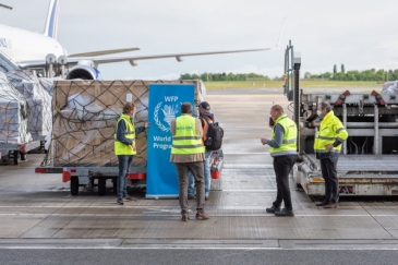 Humanitarian aid being prepared by workers for loading next to airplane.