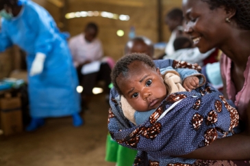 Mama akiwa amembeba bintiye mchanga akimwandaa kwa ajili ya kupata chanjo kadhaa katika kituo cha chanjo kilichofadhiliwa na UNICEF katika jimbo la Kivu Kaskazini nchini DRC.