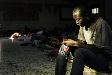 Crédits: UNICEF/UN052822/Romenzi.  Un migrant est assis près d'une source de lumière entrant par l'une des deux seules fenêtres alors qu'il tente de se réchauffer dans un centre de détention situé en Libye, le 1er février 2017. Lors de la visite de l'UNIC