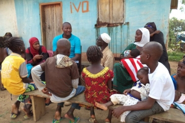 Aboubacar (wearing glasses), surrounded by his family, talks with UNICEF’s Mouctar Touré and Kadijah Diallo. (c) Léon Kamano