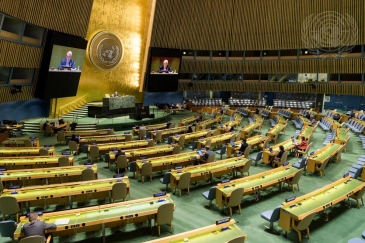 A wide view of the General Assembly Hall as Raffi Gregorian (at dais and on screens)...