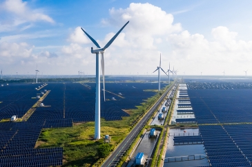 Solar panels and wind turbines with blue sky in distance.