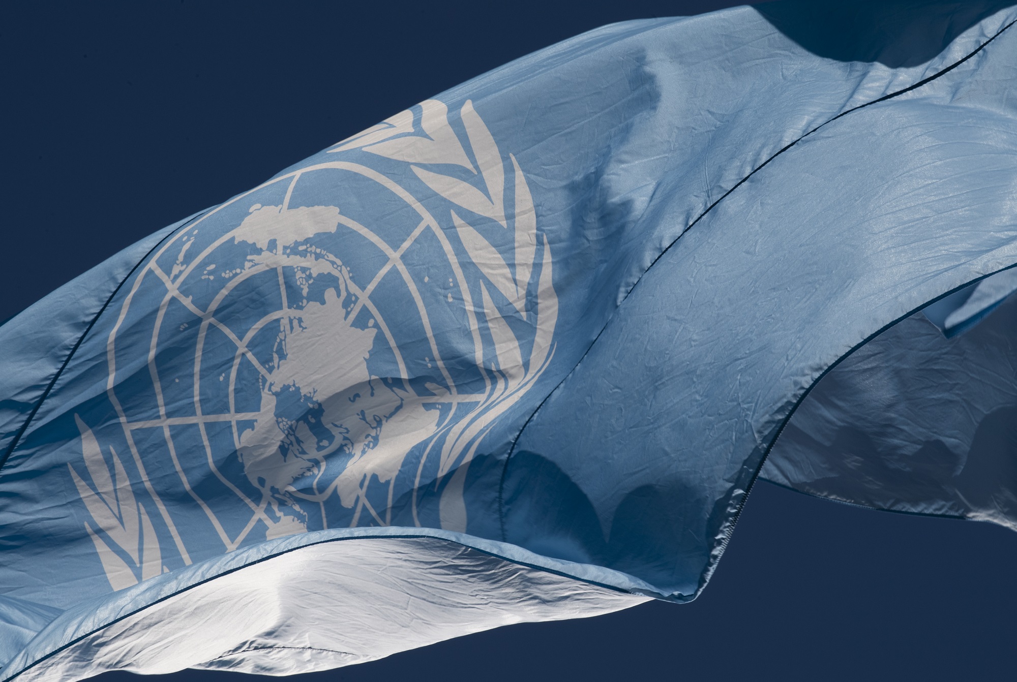 The flag of the United Nations flying -- white emblem on a light blue field.