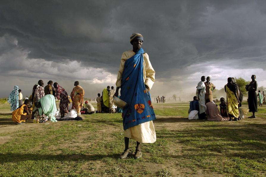 Picture of person standing on a field with clouds appearing in the background.