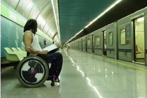 A man in a wheelchair sits at a train platform