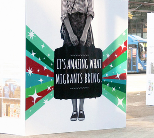 Public display of large square blocks with illustrations of individuals holding luggage with the inscription 'It's amazing what migrants bring'