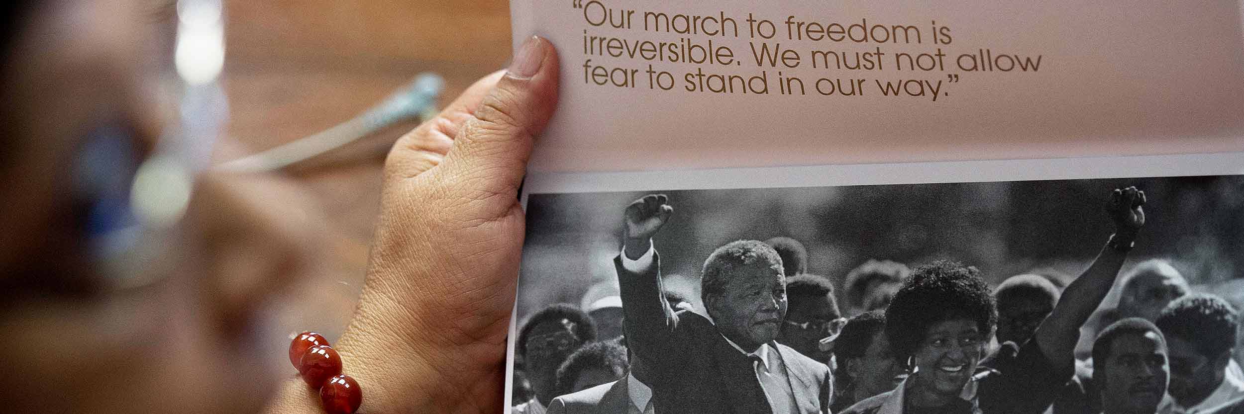 امرأة تحمل كتيبًا  عليه صورة نيلسون مانديلا ممسكًا بيد زوجه وهما محاطات بجمع غفير  