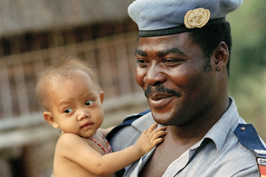 A police officer deployed to the UN Mission in Cambodia (UNTAC) visits a family in a local village, 1993.  UNTAC was one of the first complex, multidimensional UN peacekeeping operations. UN Photo/John Isaac