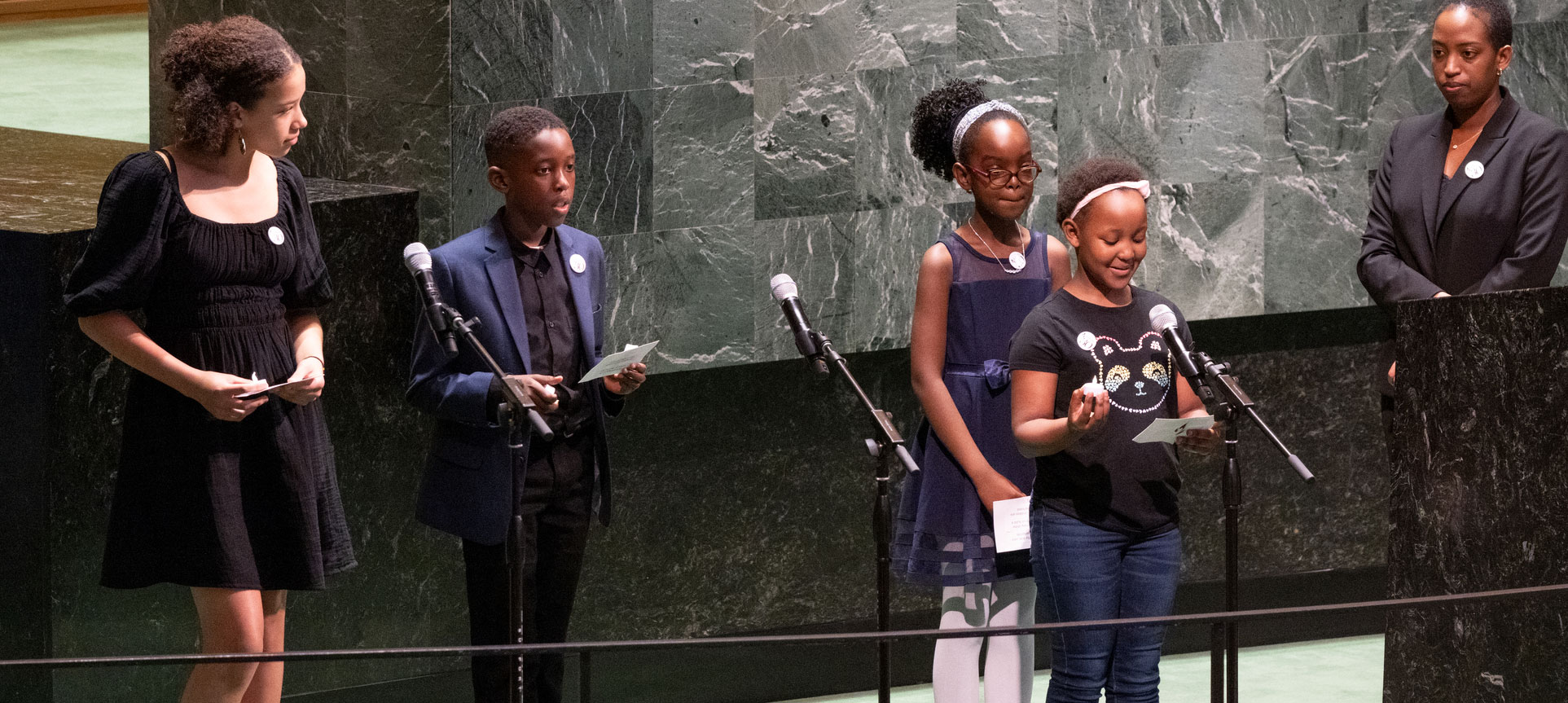 Photo d'une femme et de quatre enfants debout sur le podium dans la salle de l'AG, alors que l'un d'entre eux prend la parole.