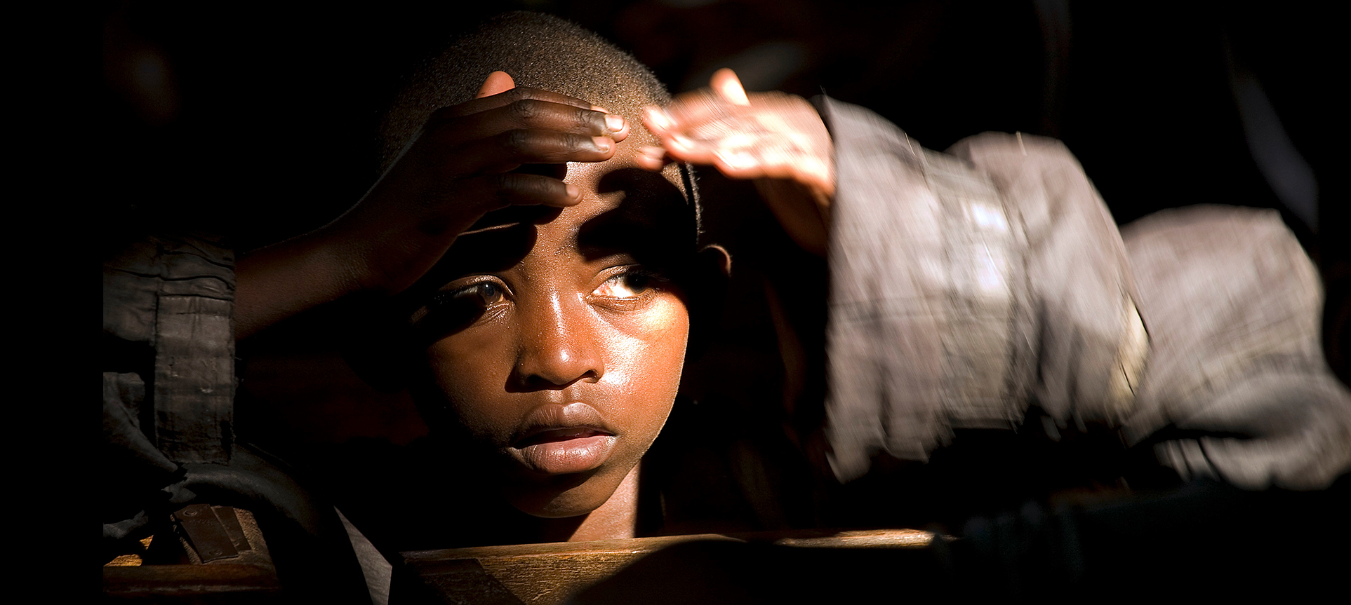 Photo of a child in a dark auditorium with his hands shielding his eyes from a beam of light.