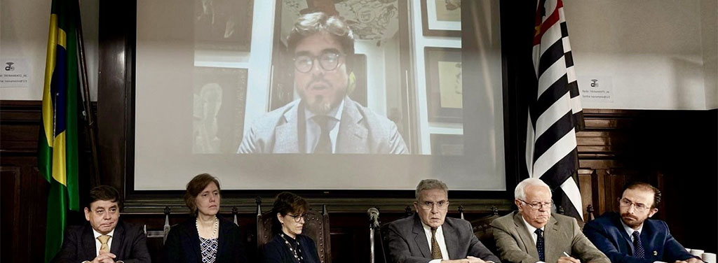 Des personnes dans une salle de réunion. Derrière elles, un écran sur lequel est projeté le message vidéo de l'ambassadeur José Javier De La Gasca