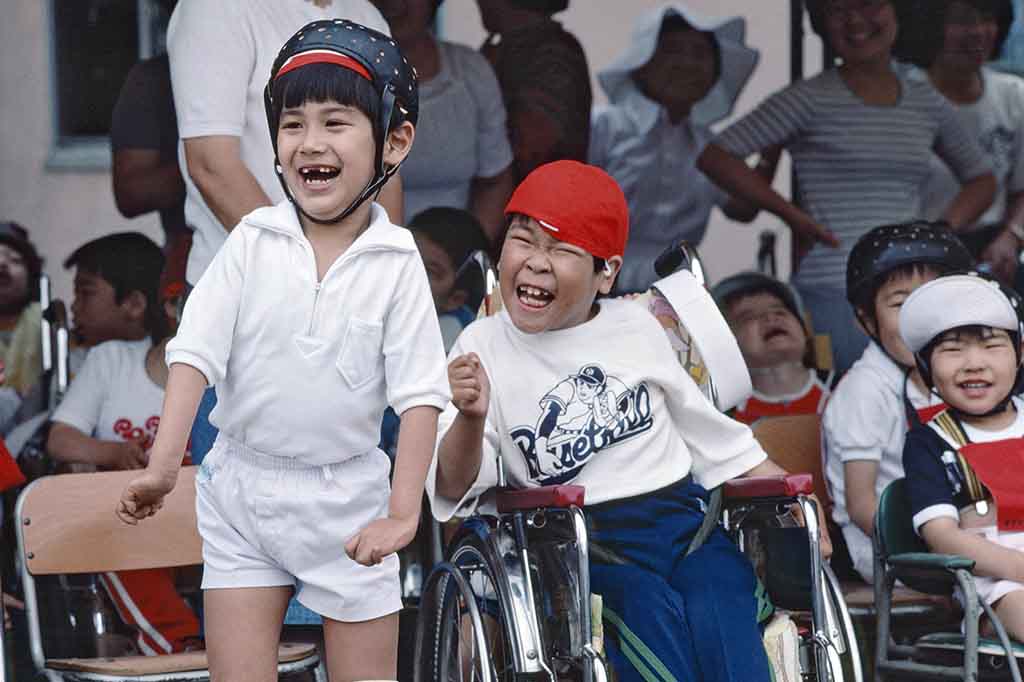 Niños con discapacidad riendo mientras asisten a un evento deportivo.