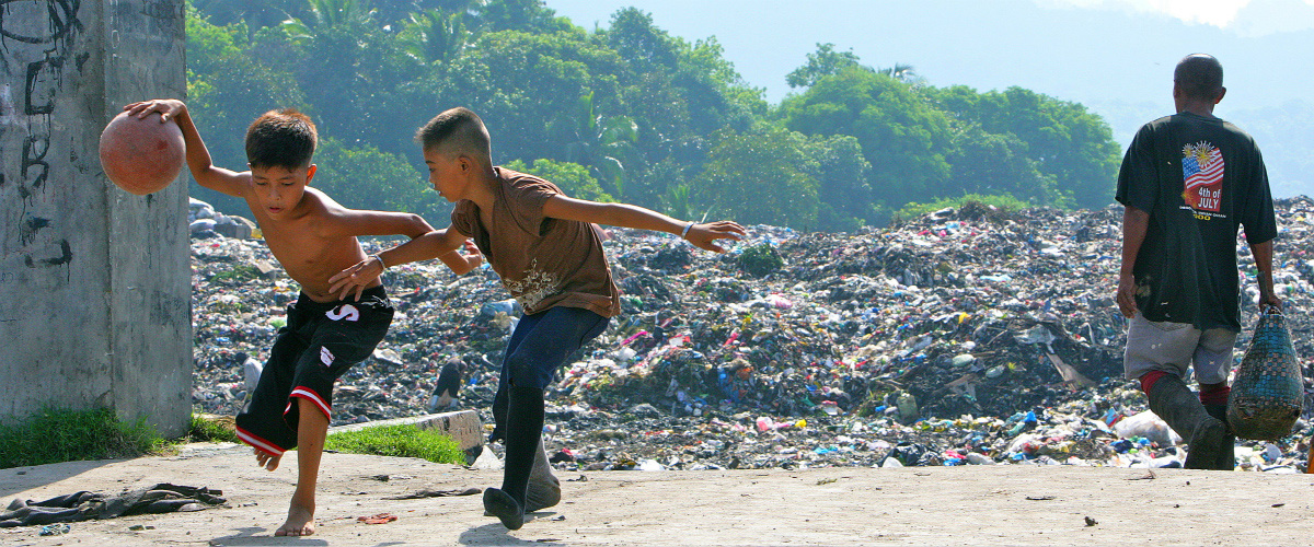 Rex (izquierda), de 14 años, juega al baloncesto con su amigo con un basurero de fondo. Lleva dos años viviendo ahí con su familia. 