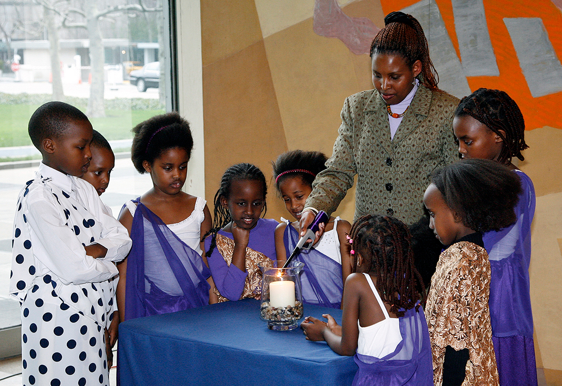 Eugenie Mukeshimana, superviviente del genocidio de Rwanda, flanqueada por niños de Rwanda, enciende una vela conmemorativa.