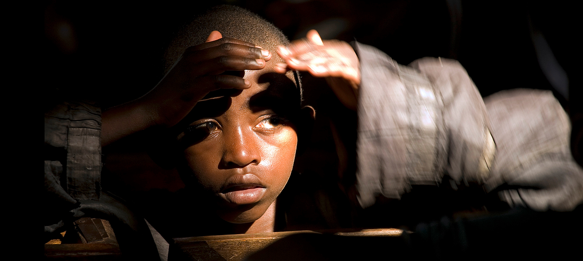 Foto de un niño en un auditorio, a oscuras, protegiéndose los ojos con las manos de un haz de luz..