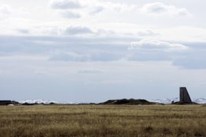 A large field runs into the distance and to the edge of a large mountainous range. There is snow on the mountaintops.