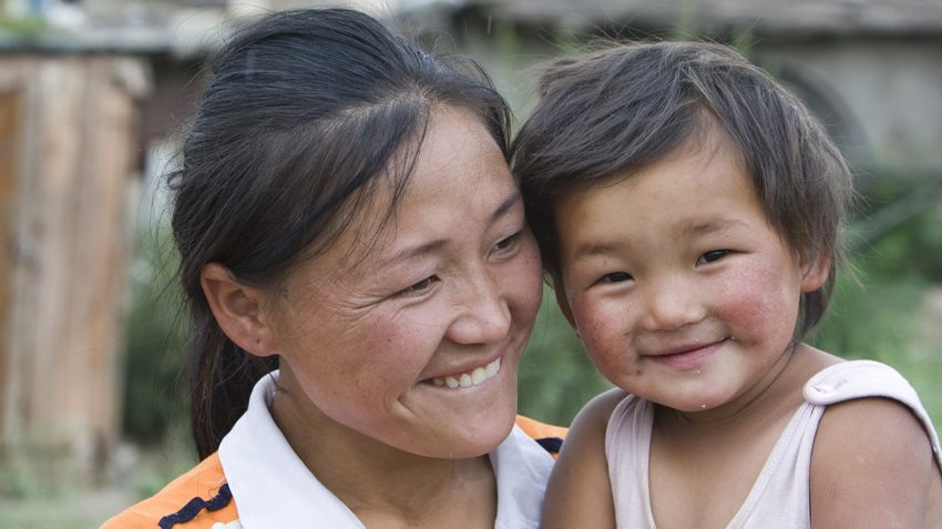 A woman bites her lip as she looks at her young child, who she is holding next to her.