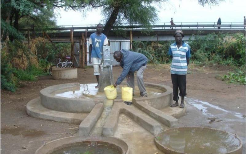 Three men are drawing water from a newly completed well.