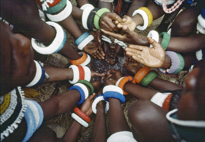 The picture shows colorfully banded arms of young men of the Ndebele tribe of South Africa engaging in an initiation ceremony.