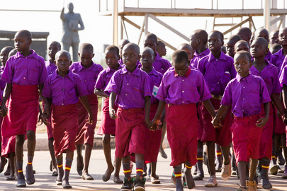The picture shows a large group of young children dressed in purple shirts and red trousers.