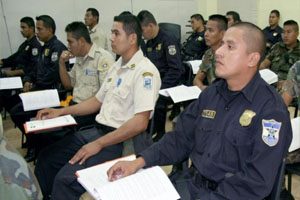 Police dressed in their official uniforms sit at wooden desks. On their desks are various documents that form part of the training course.