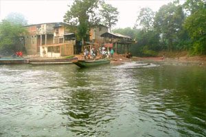 A river wraps around a group informal settlements. There is a canoe floating in the river, with several individuals watching on.