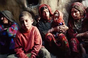 Three older woman sit in a dark space. They have concerned facial expressions. There are two children sitting between the women.