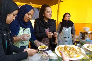 Women stand in front of a table and serve food.