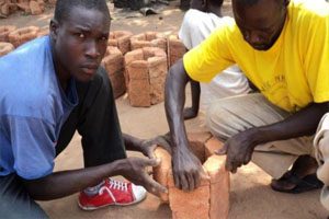 Two men are building kneeling on the floor to and are building a stove.