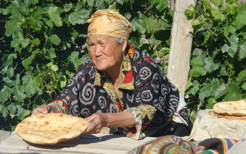 An old woman leans over a wooden table holding a round piece of baked bread.
