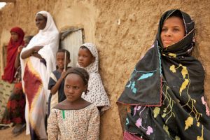 Malian girls stand in the shade in Kidal, northern Mali. Two older women stand near the younger girls with their arms crossed.