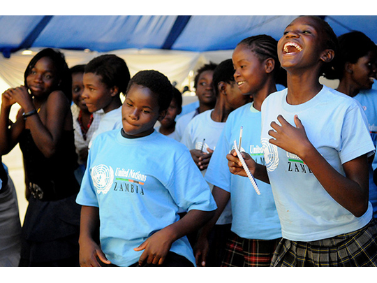 A group of smiling children are wearing blue shirts stating: “United Nations Zambia” shirt.