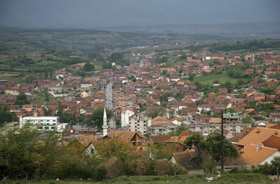 The image is taken on a green hill overlooking a small town and runs off into the distance. All the tiled rooftops are orange and red tones.