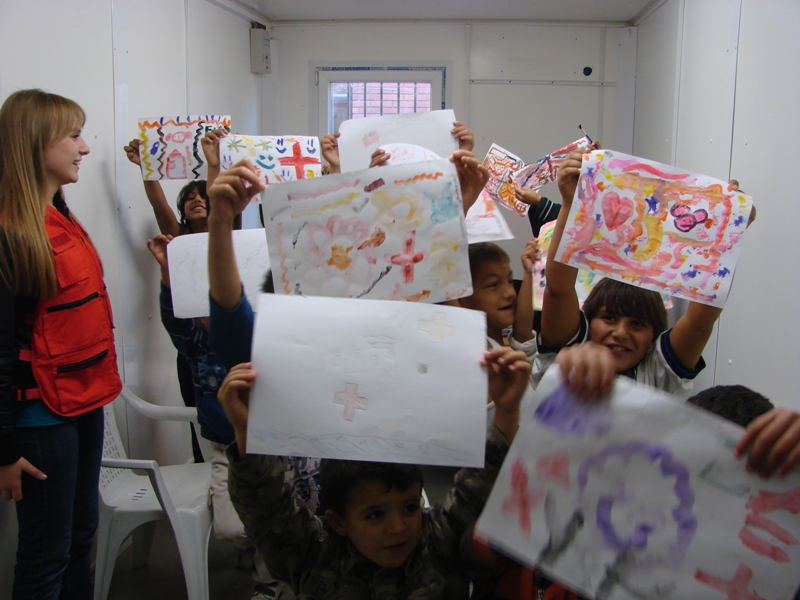 Several children hold up colourful paintings they have drawn to the camera.