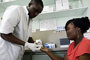 A woman is sitting in a chair holding her hand up for inspection by a male doctor in a white coat. They are sitting in a doctor’s office at a medical centre.
