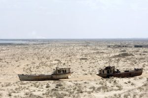 Two ships lie stranded in a vast field. There are small houses and powerlines in the background.