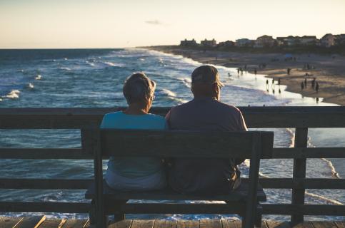 Two older people watching the sunset from a bench